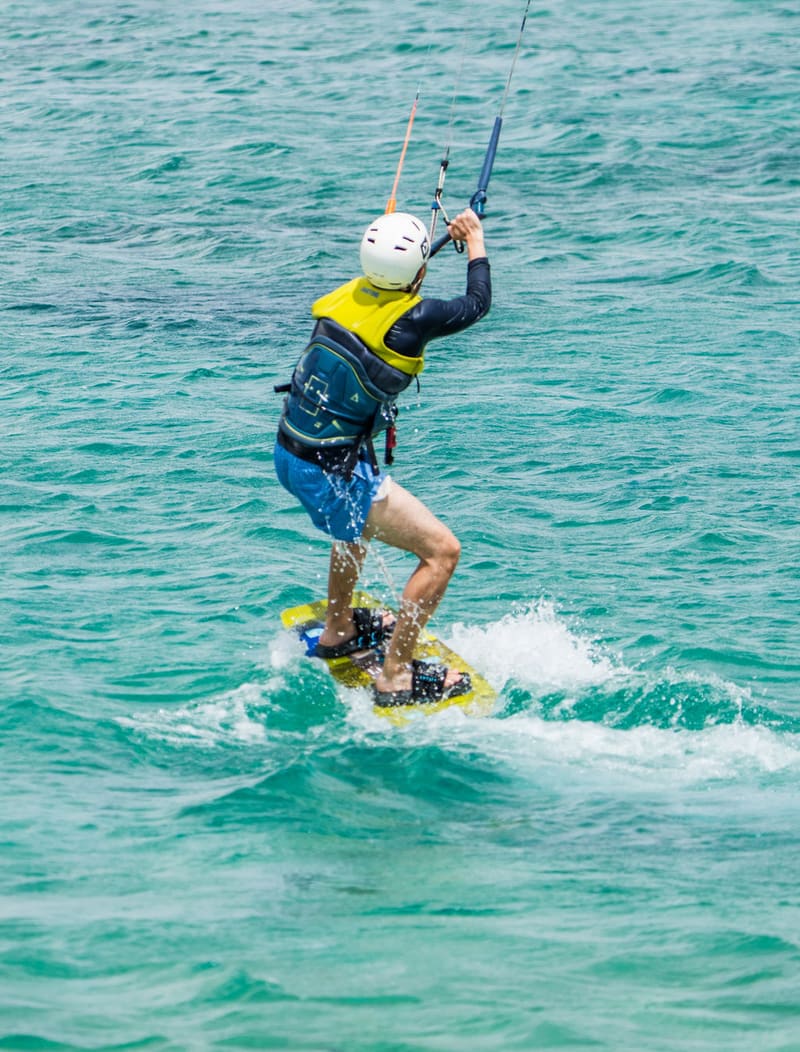 Kitesurfista de capacete e colete velejando em água turquesa