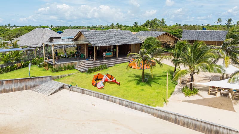 A escola vista do alto, dentro do Bar.Co: cabanas, gramado e kites na beira da praia