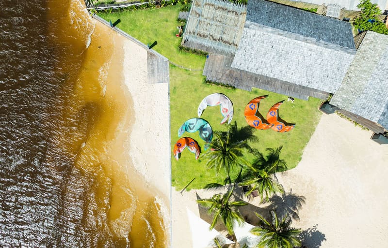 A escola vista do alto, com os kites no gramado, na beira do Rio Preguiças, em Atins