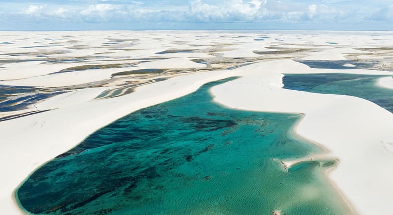 Vista aérea das dunas brancas e de uma lagoa verde-azulada nos Lençóis Maranhenses